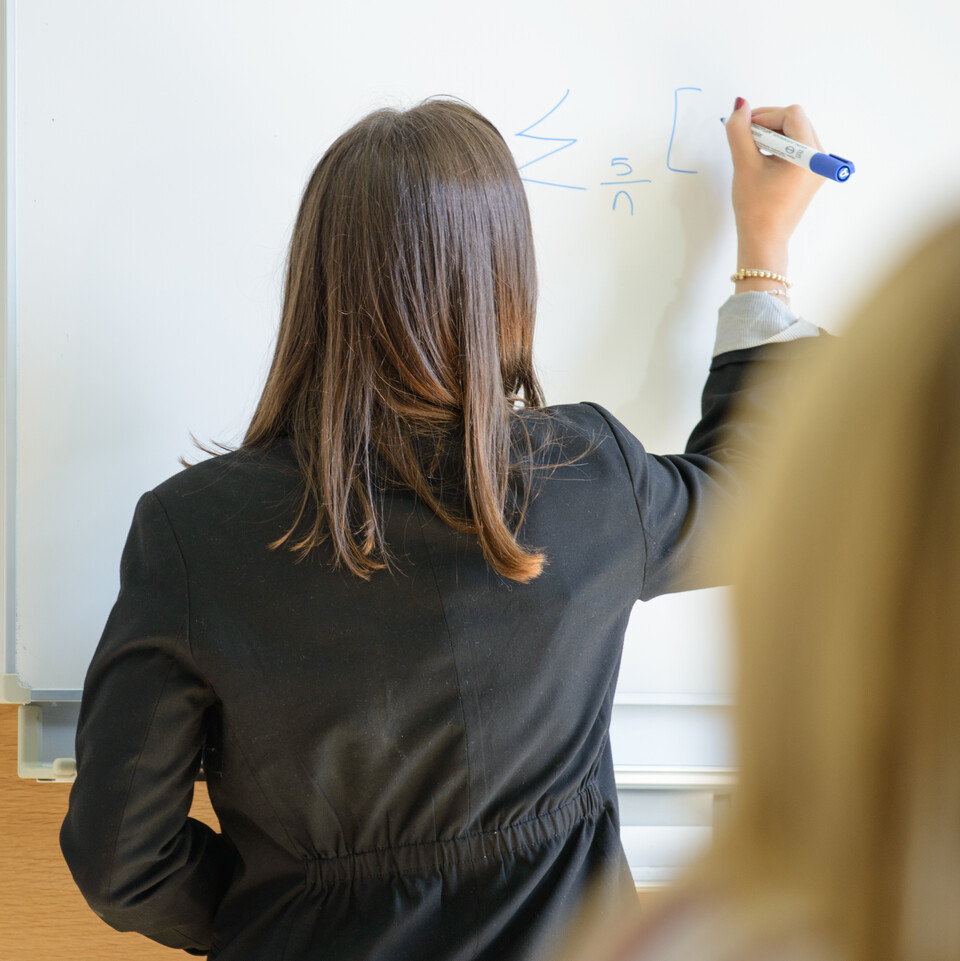 Eine Dozentin schreibt etwas an eine Tafel.
