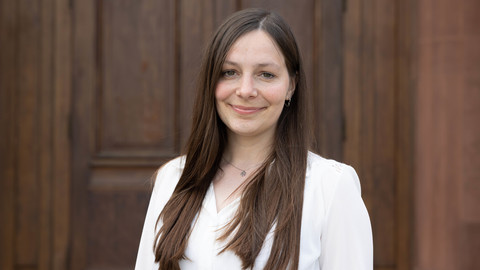 Fabienne Unkelbach. She is wearing a white shirt and is standing in front of a brown door.