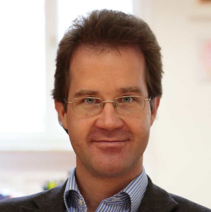 Prof. Dr. Christian Mann mit kurzen braunen Haare, einer eckigen Brille in einem blau-weiß-gestreiftem Hemd und anthrazit-farbenen Sakko in einem Büro