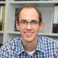Portrait von Thorsten Meiser. Er trägt eine Brille und ein blau-weiß kariertes Hemd. 