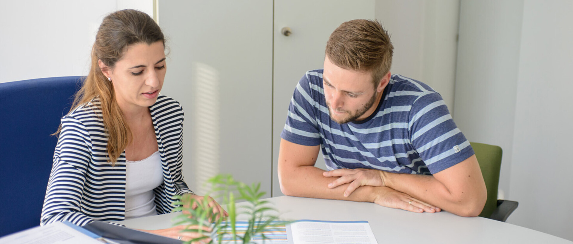 Eine Mitarbeiterin zeigt einem Studenten eine Broschüre.