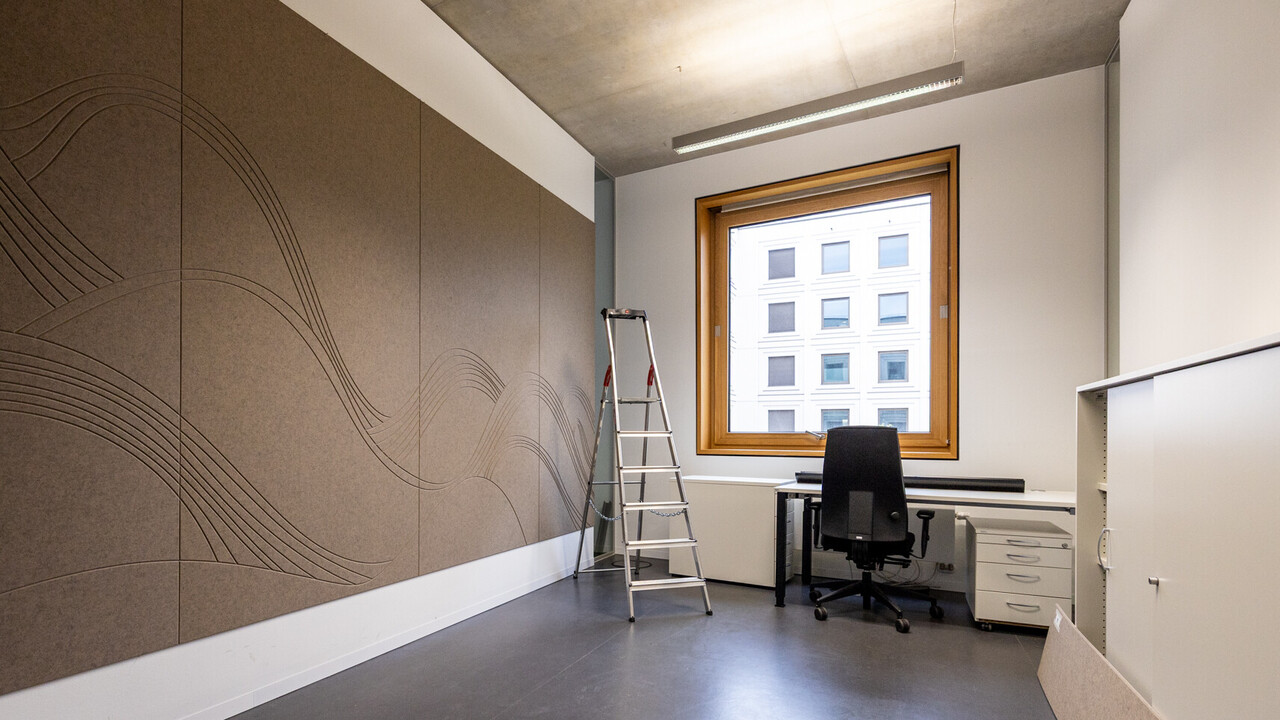 Das Bild zeigt einen Einzel-Büroraum. Er wird gerade eingerichtet. An der Wand ist eine große braune Filzwand angebracht. Sie dient der Schalldämmung und ist mit Wellen dekoriert.
