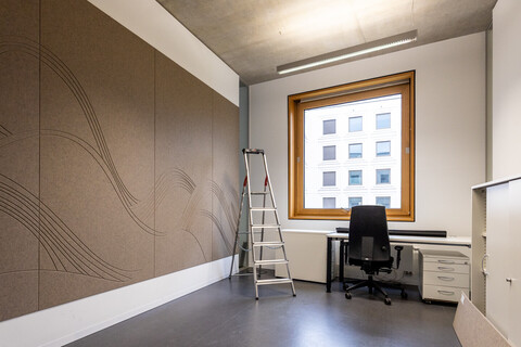 Das Bild zeigt einen Einzel-Büroraum. Er wird gerade eingerichtet. An der Wand ist eine große braune Filzwand angebracht. Sie dient der Schalldämmung und ist mit Wellen dekoriert.