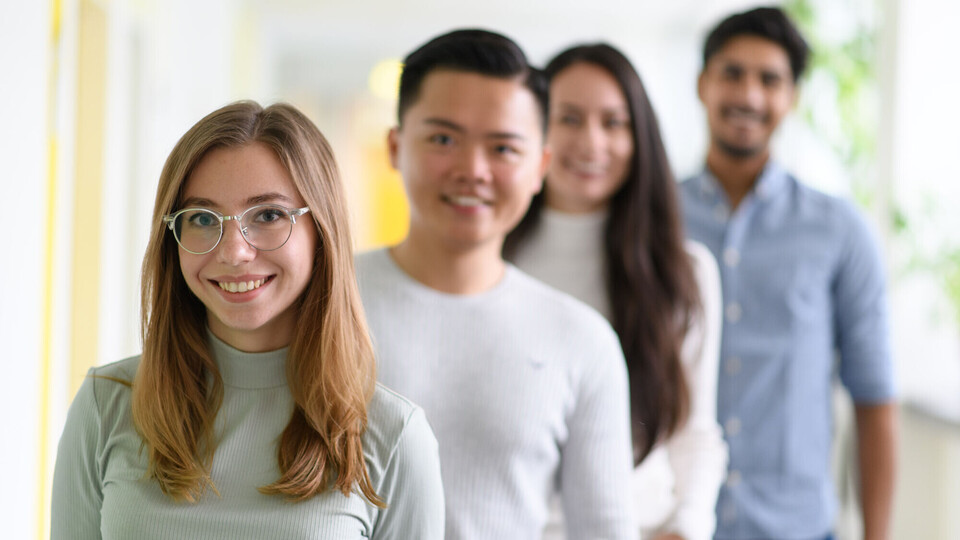 Mehrere Studierende stehen hintereinander aufgereiht und lächeln.