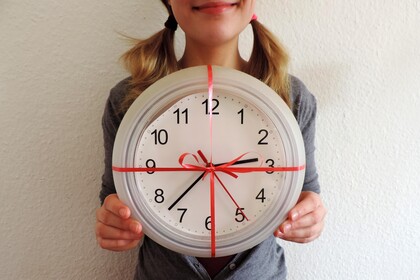 Eine Frau hält eine gebastelte Uhr in den Händen, die mit roten Geschenkband eingepackt ist.