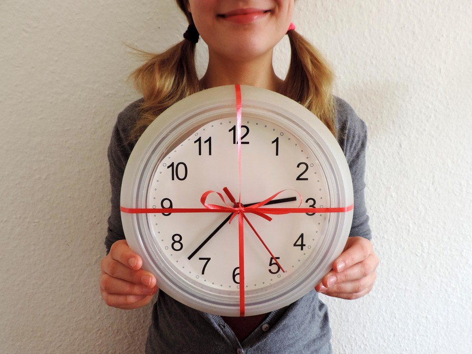 Eine Frau hält eine gebastelte Uhr in den Händen, die mit roten Geschenkband eingepackt ist.