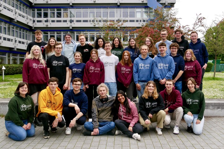 Ca. 30 Mitglieder der Fachschaft Soziologie und Politikwissenschaft stehen für ein Gruppenfoto vor dem A5-Gebäude. Sie tragen verschiedenfarbige, bunte Hoodies.
