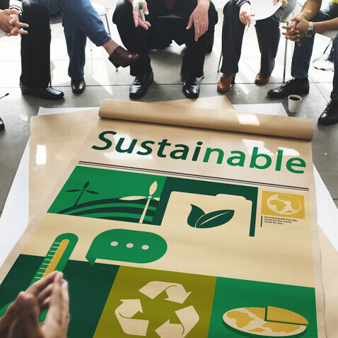 Mehrere Menschen sitzen um ein Plakat herum, auf dem "Sustainable" steht. 