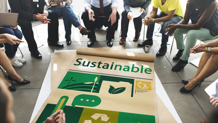 Mehrere Menschen sitzen um ein Plakat herum, auf dem "Sustainable" steht.