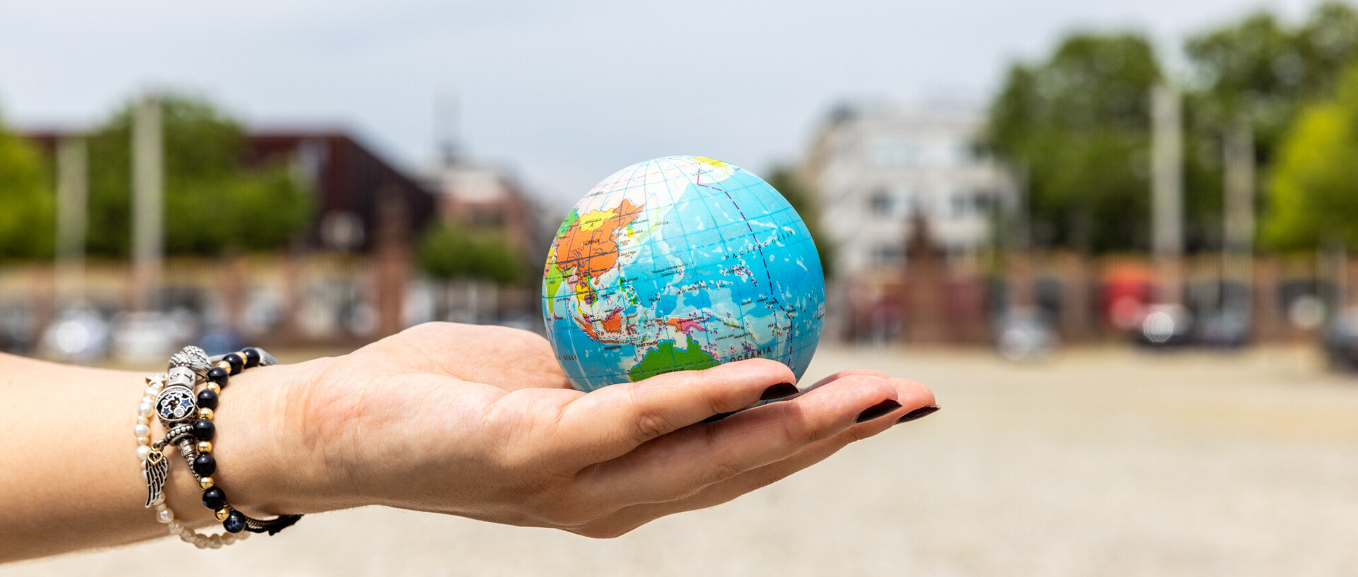 Student holding a globe in the palm of her hand. She is wearing three bracelets in black and silver and has black nail polish.