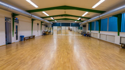 Große Sporthalle mit braunem Parkettboden und Spiegelwand im Hintergrund.