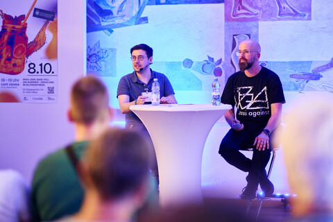 Der Moderator und Prof. Paulheim sitzen an einem Stehtisch und sprechen bei WISSENsdurst vor Publikum.