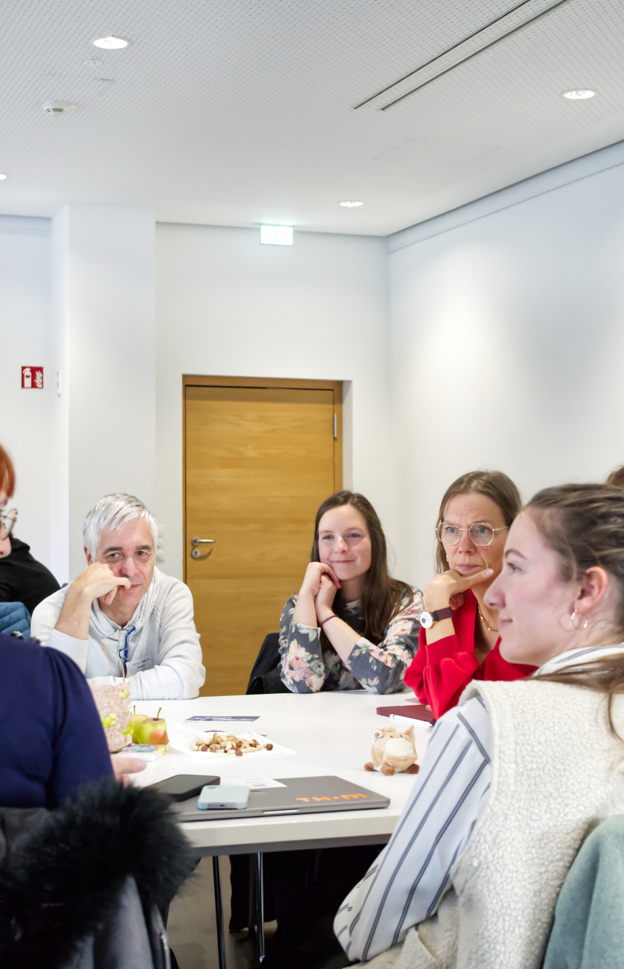 Vier Teilnehmende blicken fröhlich und interessiert zu einer Person außerhalb des Bildes und sitzen gemeinsam um einen Tisch herum.