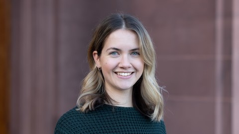 Klara Müller. She is wearing a black sweater and is standing in front of a brown stonewall.