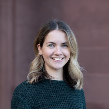 Klara Müller. Sie trägt einen schwarzen Pullover und steht vor einer Steinwand.