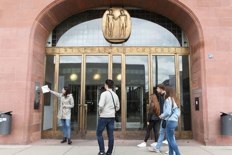 Studierende bei einer Führung vor dem Haupteingang der Universität Mannheim mit der Aufschrift "Wirtschaftshochschule".