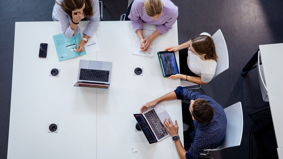 Mehrere Personen sitzen mit Laptops an einem Tisch.