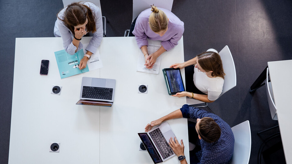 Vier Forschende an der Uni Mannheim sitzen an einem Tisch mit Laptops und Tablets.