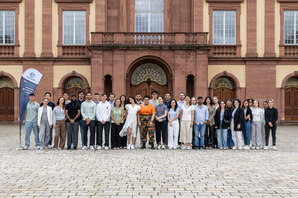 Gruppenbild von Studierenden, die im Ehrenhof des Schlosses Mannheim nebeneinander stehen und in die Kamera blicken.
