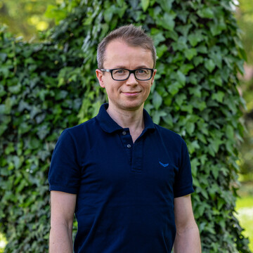 Dr. Peter Parczewski in dunkelblauem Poloshirt vor einem Hintergrund mit grünen Pflanzen und Bäumen.