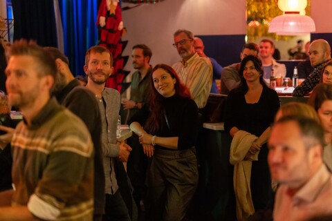 Mehrere Personen stehen in einer Bar und schauen in eine Richtung.
