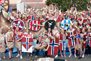 Etwa 30-40 Menschen, die als Wikinger verkleidet sind, stehen vor einem aus Pappe gebastelten Wikingerboot. Sie tragen Wikingerhelme mit zwei Hörnern und viele die norwegische Flagge als Gewand.