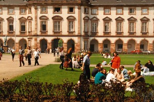 alte Aufnahme der Mensawiese der Universität Mannheim. Viele Studierende sitzen auf der Wiese oder laufen auf dem Gelände herum.