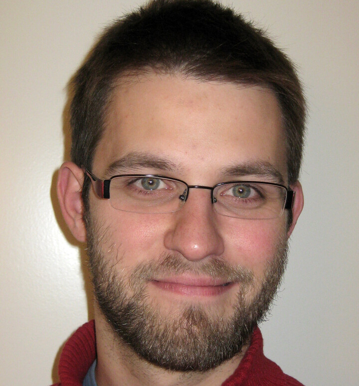 Portrait von Stefan Janke. Er trägt einen roten Rollkragenpullover und lächelt.