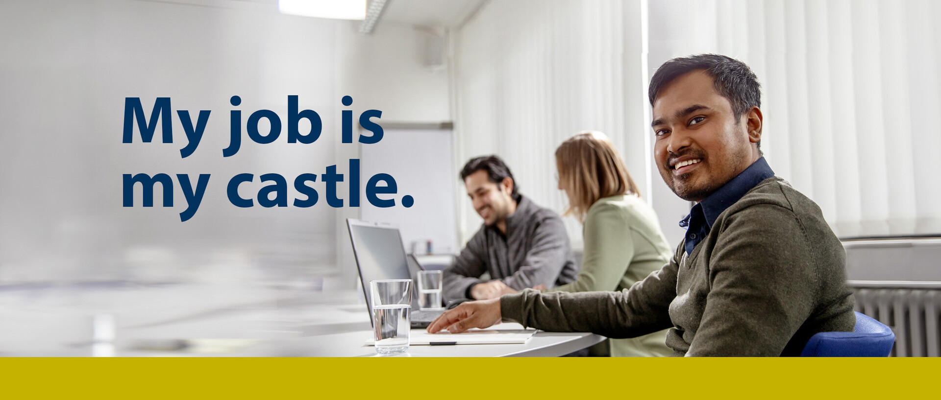 Foto mit Text: Drei Personen sitzen nebeneinander und gut gelaunt vor Laptops an Tischen. Text: My job is my castle.
