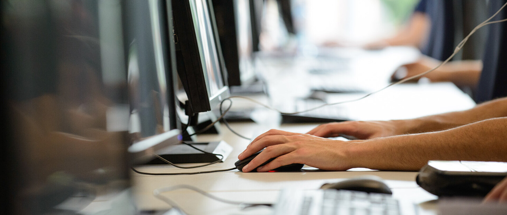Vier Menschen sitzen in einer Reihe vor Computern.