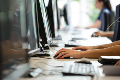 Vier Menschen sitzen in einer Reihe vor Computern.