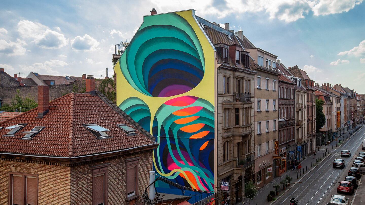 Buntes Graffiti Häuserwand in der Mannheimer Neckarstadt West vor blauem Himmel.