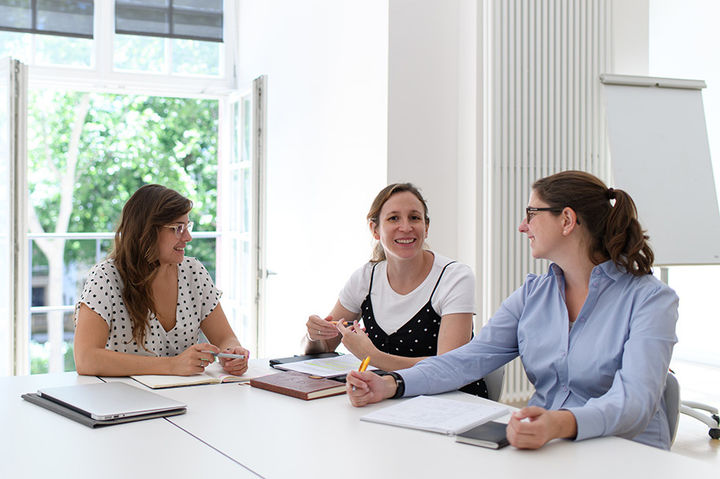 Drei Frauen sitzen in einem Seminarraum und führen ein Gespräch.