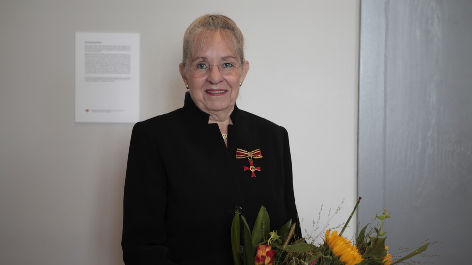 Dorothee Dickenberger steht vor einer Wand und hält einen Strauß Blumen in der Hand.