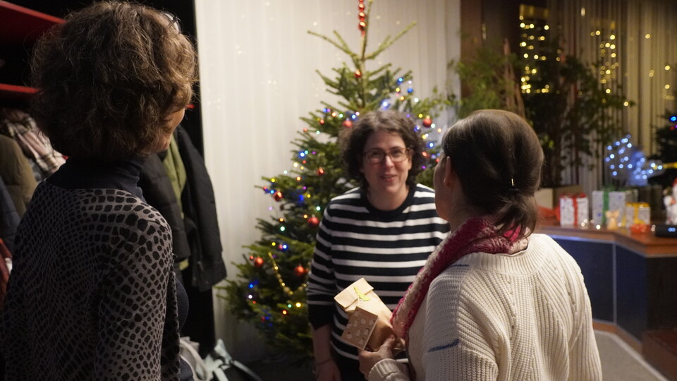 Zufällige Aufnahme eines Gesprächs zwischen drei Personen. Im Hintergrund ein geschmückter und beleuchteter Weihnachtsbaum.