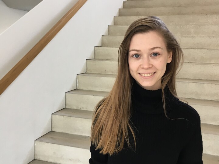 Junge Frau mit langen glatten Haaren und schwarzem Pullover im Treppenhaus