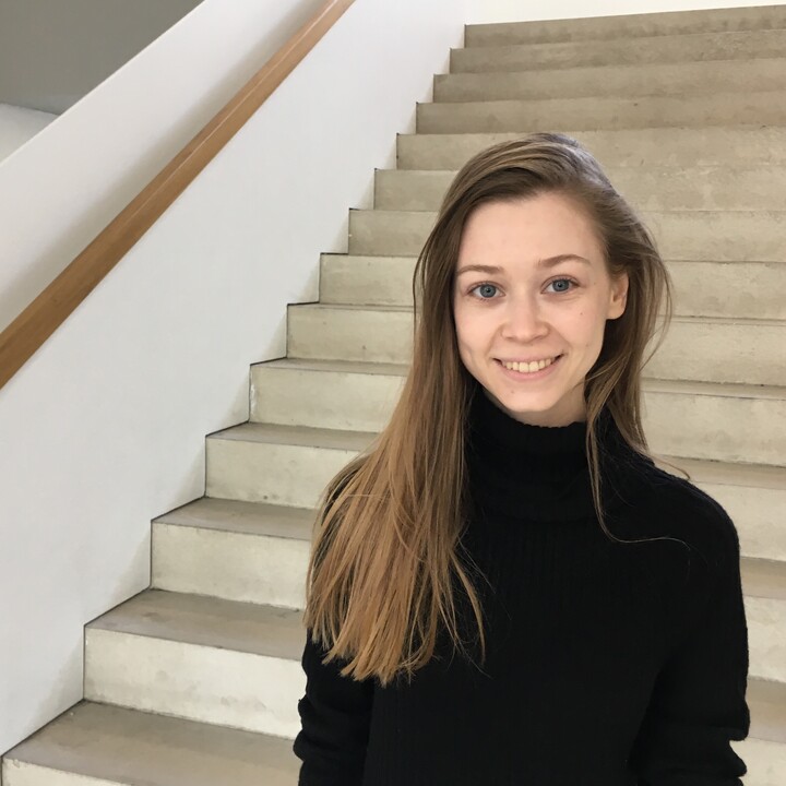 Junge Frau mit langen glatten Haaren und schwarzem Pullover im Treppenhaus