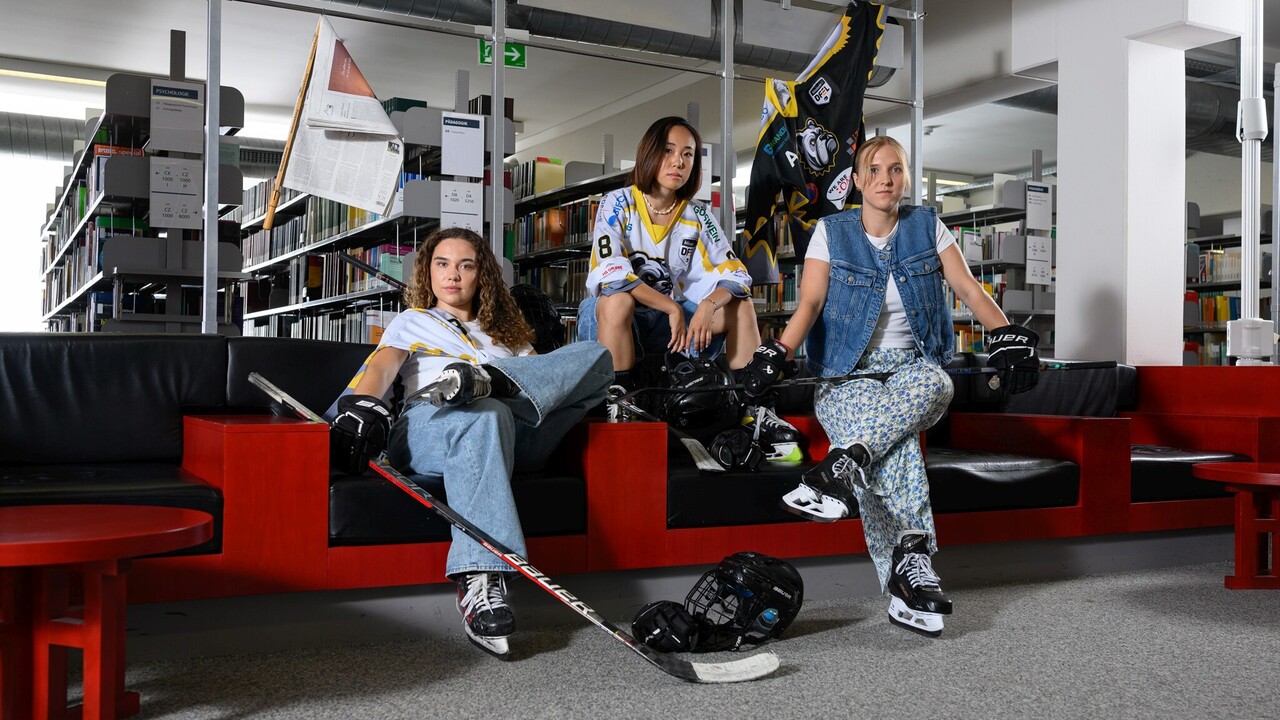 Drei Sportlerinnen in Eishockey-Ausrüstung sitzen in der A3 Bibliothek.