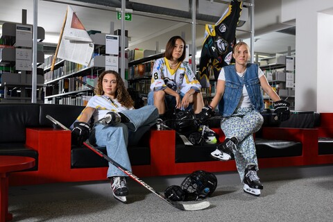 Drei Sportlerinnen in Eishockey-Ausrüstung sitzen in der A3 Bibliothek.