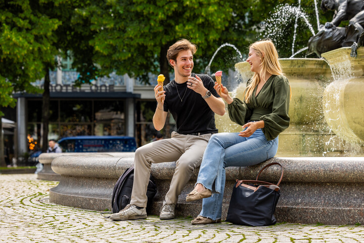 Zwei Studenten sitzen am Brunnen am Paradeplatz. Sie essen Eis und scheinen gute Laune zu haben.