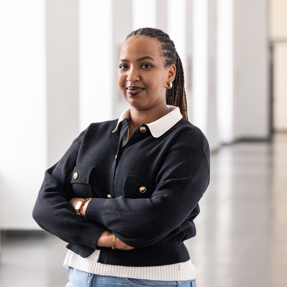 Portrait von Aurore Zoé Ikirezi Akuzweyezu. Sie trägt eine weiße Bluse und eine schwarze Jacke mit goldenen Knöpfen.