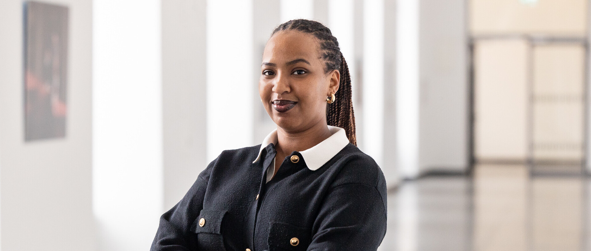 Portrait von Aurore Zoé Ikirezi Akuzweyezu. Sie trägt eine weiße Bluse und eine schwarze Jacke mit goldenen Knöpfen.