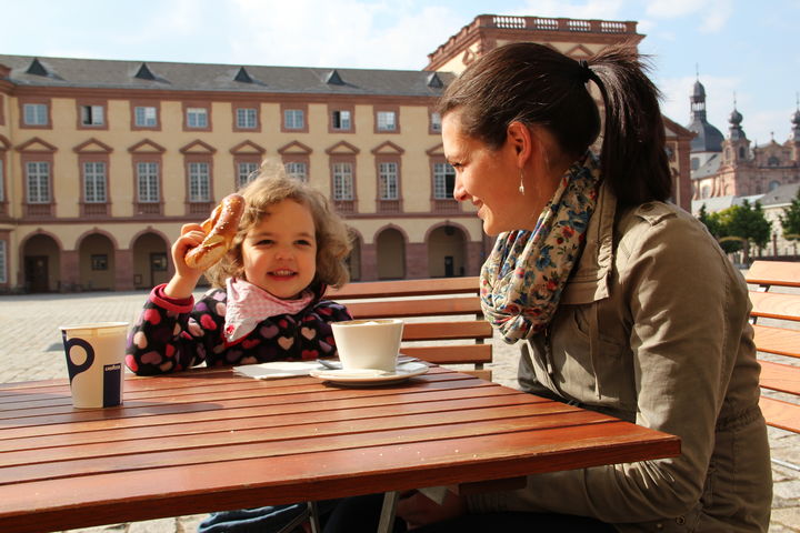 A woman and a child on the Ehrenhof, drinking coffee and eating a pretzel.