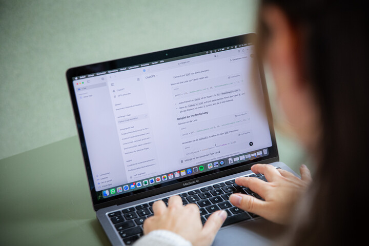 Eine Person ist von hinten zu sehen, wie sie am Laptop arbeiten und ChatGPT zum Arbeiten nutzt.