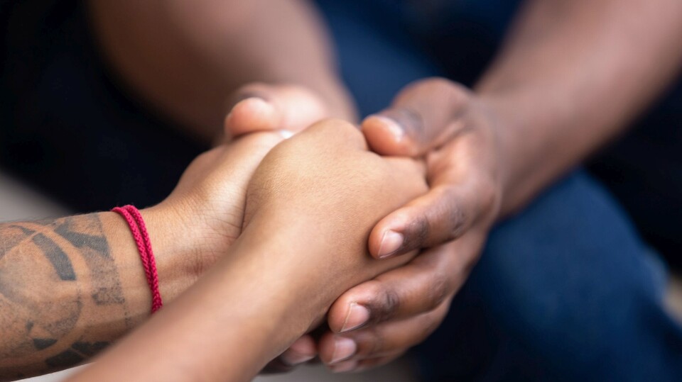 Die gefalteten Hände einer Person werden von den Händen einer zweiten Person umschlossen