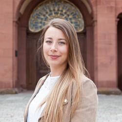 Anna Wildhirt has long blond hair. She is wearing a beige jacket with a white blouse underneath.