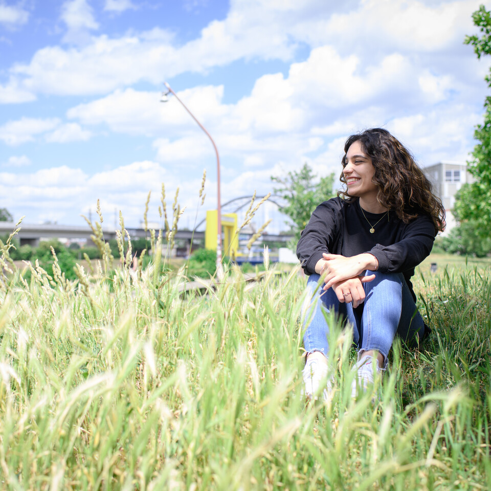 Eine Person sitzt auf einer Wiese und es ist gutes Wetter mit Sonnenschein und leichten Wolken.
