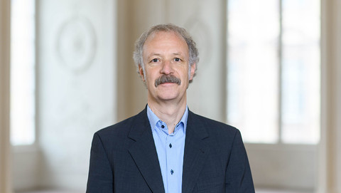 Prof. Dr. Moritz Fleischmann hat graue Haare und einen Schnauzer. Er trägt ein dunkles Jackett und ein gestreiftes Hemd.