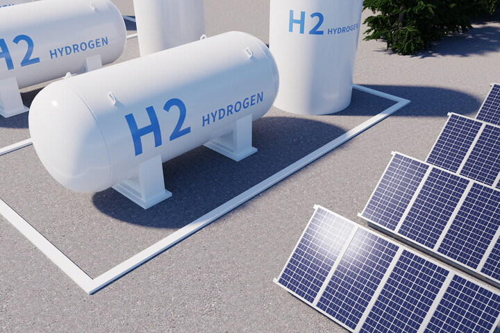 Weiße Wasserstofftanks mit der Aufschrift 'H2 Hydrogen' stehen neben Solarpaneelen auf einem Asphaltboden.