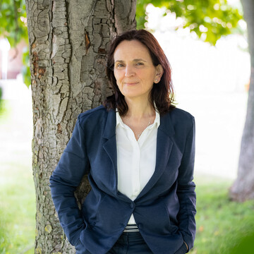  María Jesús Collado. Sie lehnt freundlich dreinblickend an einem Baum. Sie trägt einen dunkelblauen Anzug.